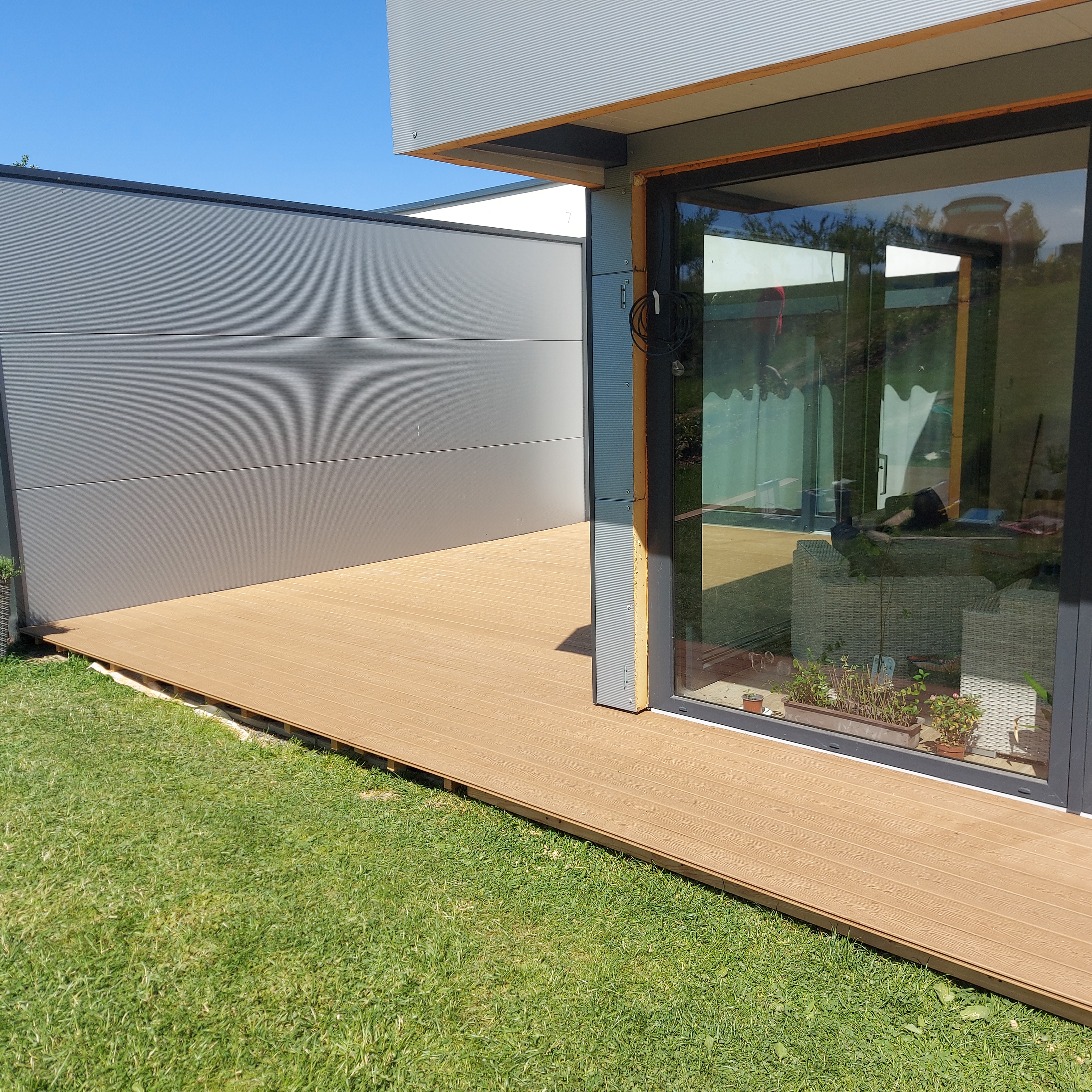 Světlá WPC terasa u moderního domu s prosklenou stěnou